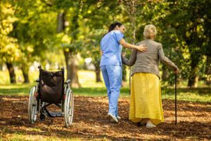 Caregiver calmly helps an older resident choose clothing in a bright assisted living room.
